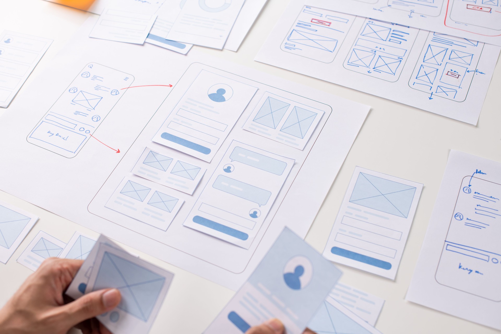 UX/UI designer working on wireframes for a website and mobile app prototype, surrounded by sketches of user-flow and design tools, in concept of website and mobile application design concept.